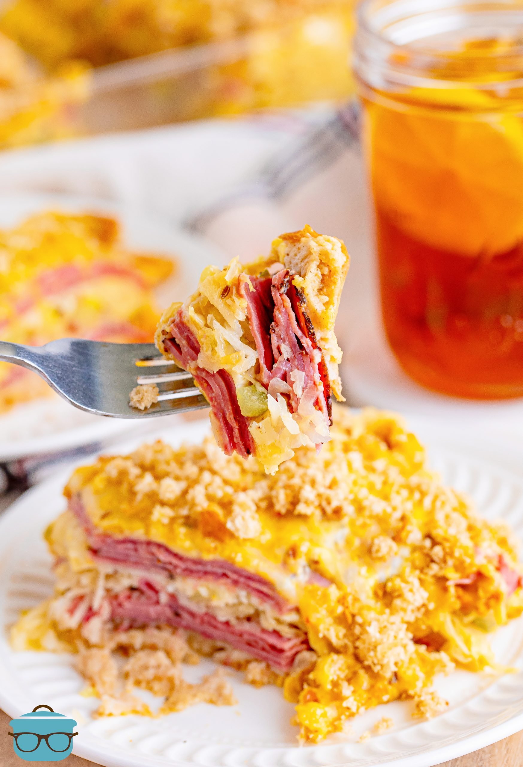 A fork holding a bite of Reuben Casserole above a plate with a serving of it.