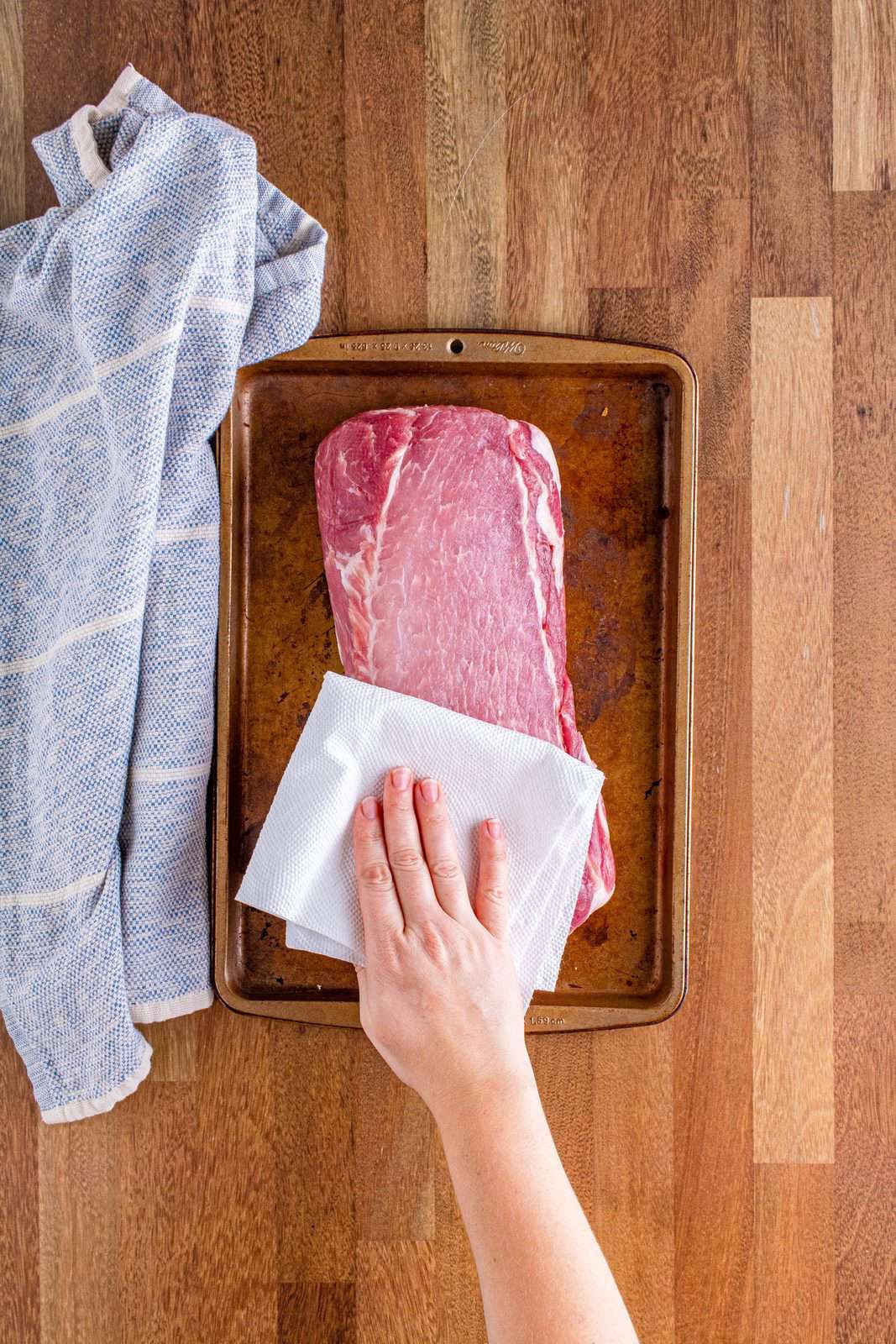 a hand holding a paper towel and patting dry a pork roast.