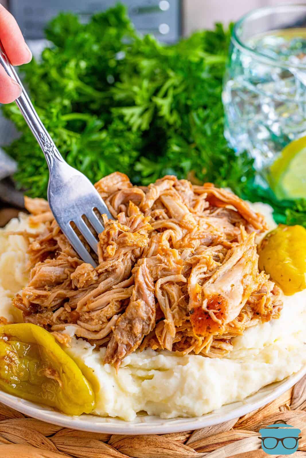 A fork shown inside shredded pork that is on top of mashed potatoes on a plate. 