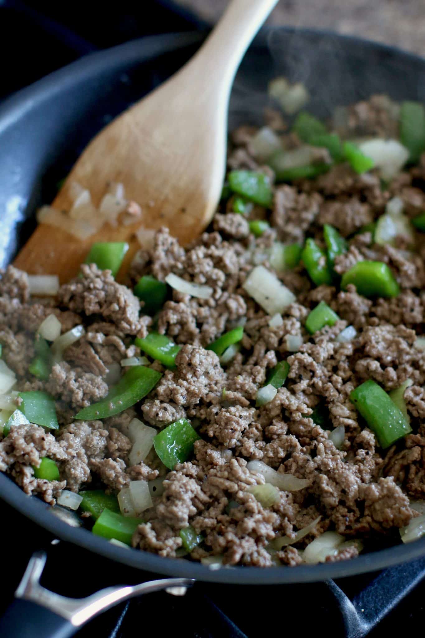 cooked ground beef with onions and green peppers in a skillet. 