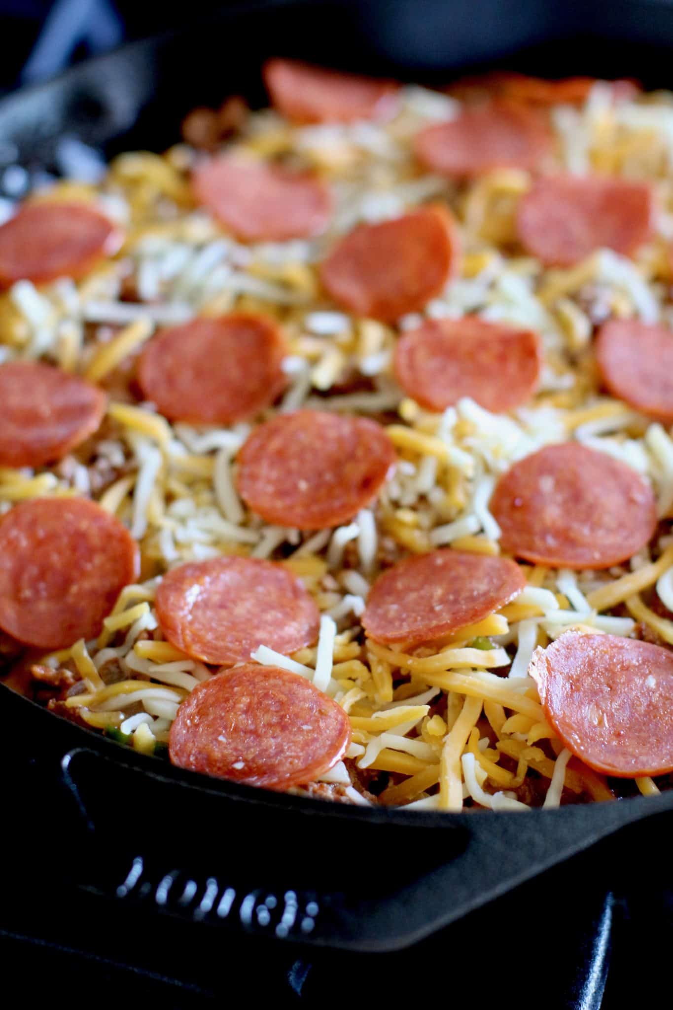 shredded cheese and sliced pepperoni slices on top of pizza in the skillet. 