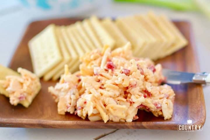 Pimiento Cheese shown on a wooden square dish with club crackers.