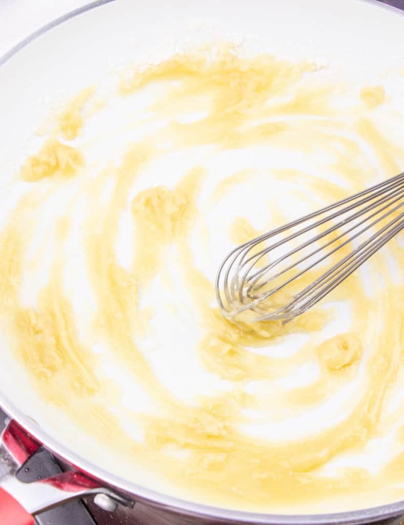 making a roux with flour and butter using a whisk in a skillet