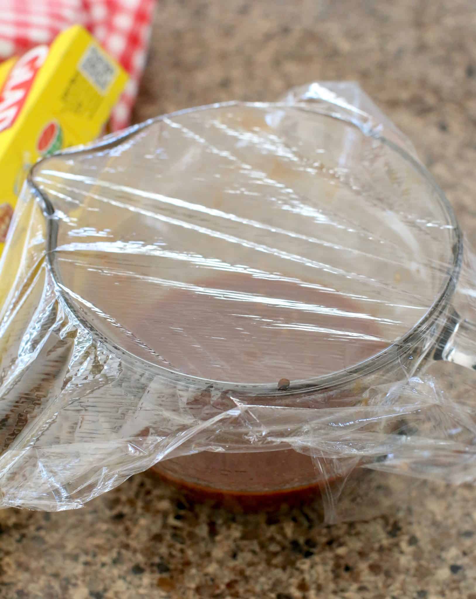 BBQ sauce in a clear bowl topped with plastic wrap.