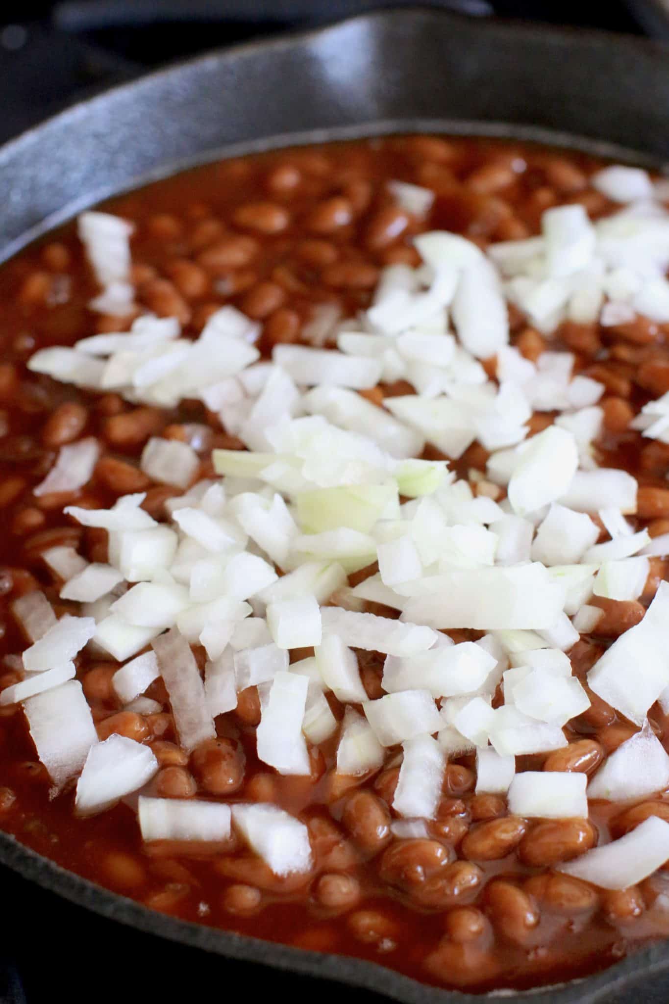 diced onion on top of beans in a skillet. 