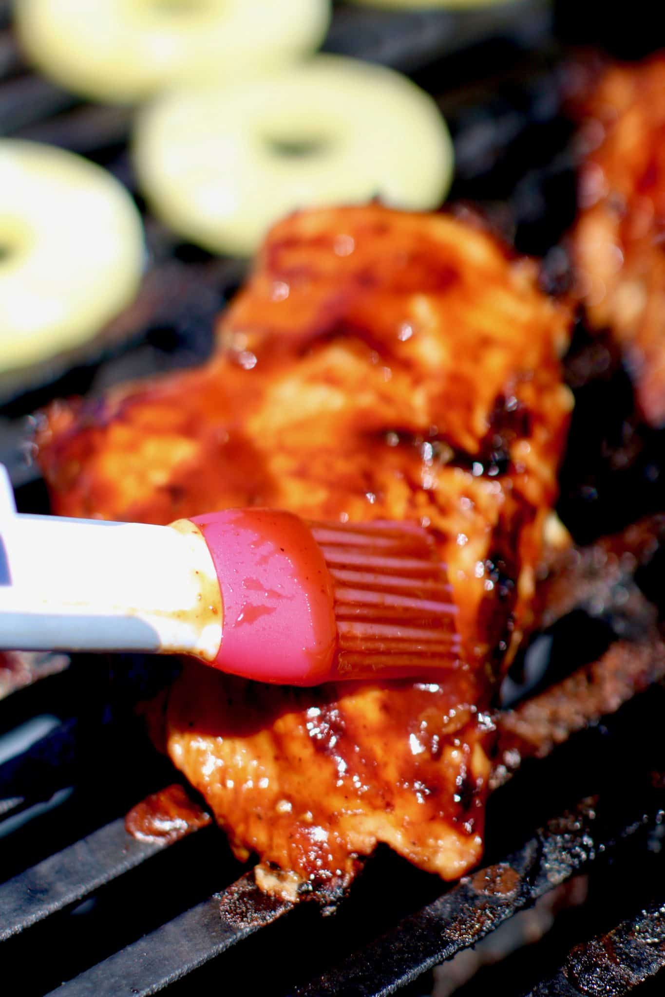 a pastry brush being shown brushing on bbq sauce on the grilled chicken. 