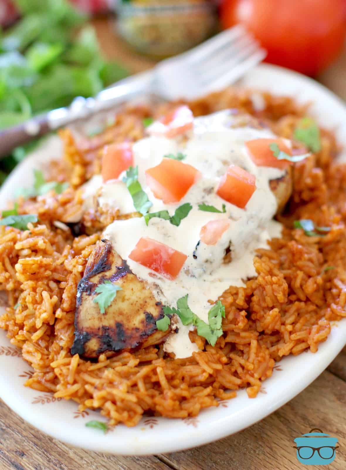 Mexican rice on an oval plate and topped with grilled lime chicken and queso sauce drizzled on top.