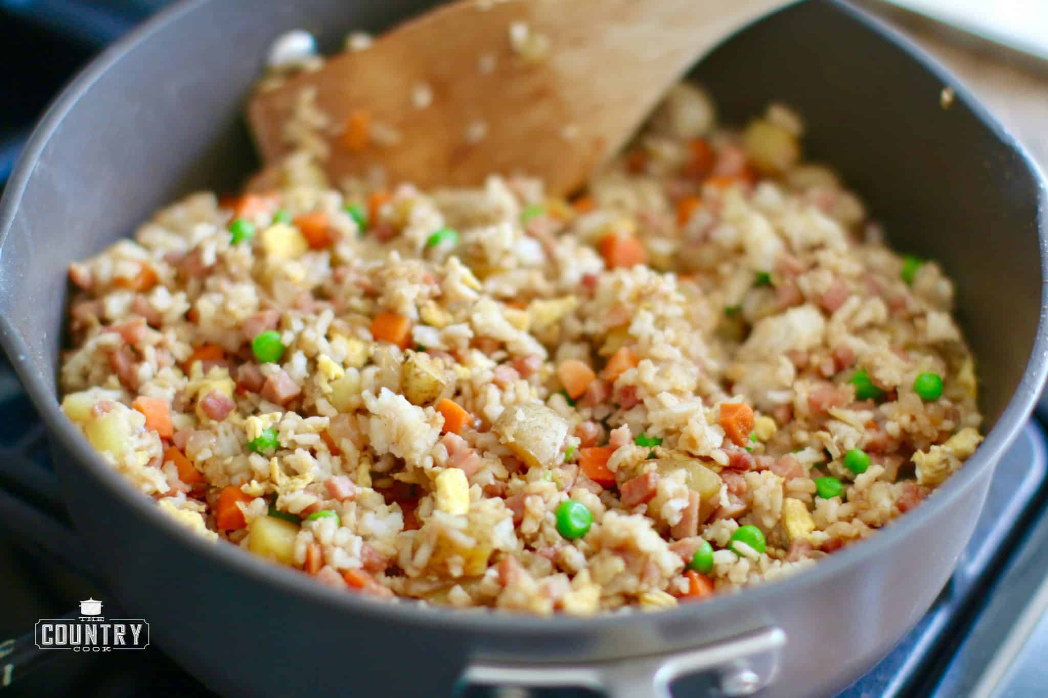 Potato and Ham Fried Rice shown in a large skillet with a wooden spatula.