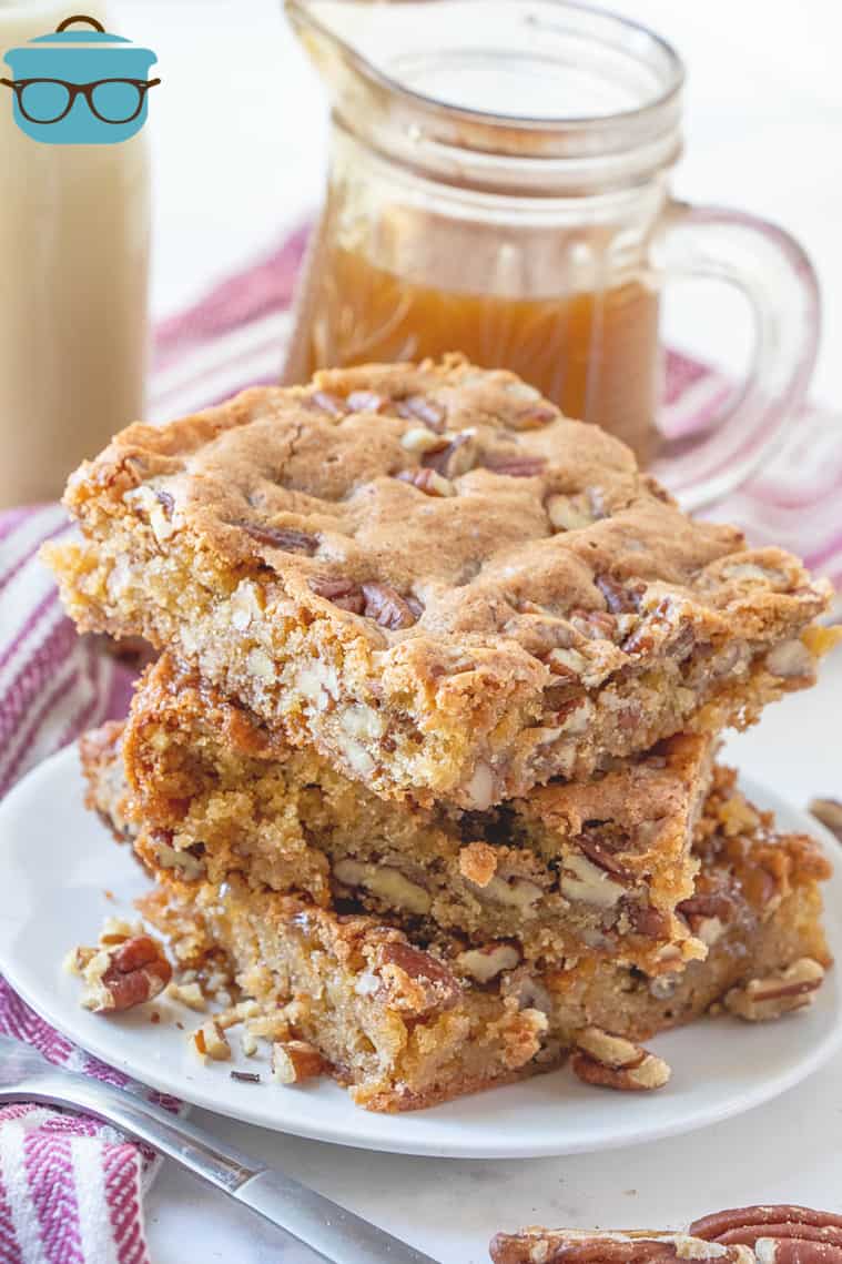 Southern Pecan Cake Bars, stacked on a white plate with a jar of caramel sauce in the background.