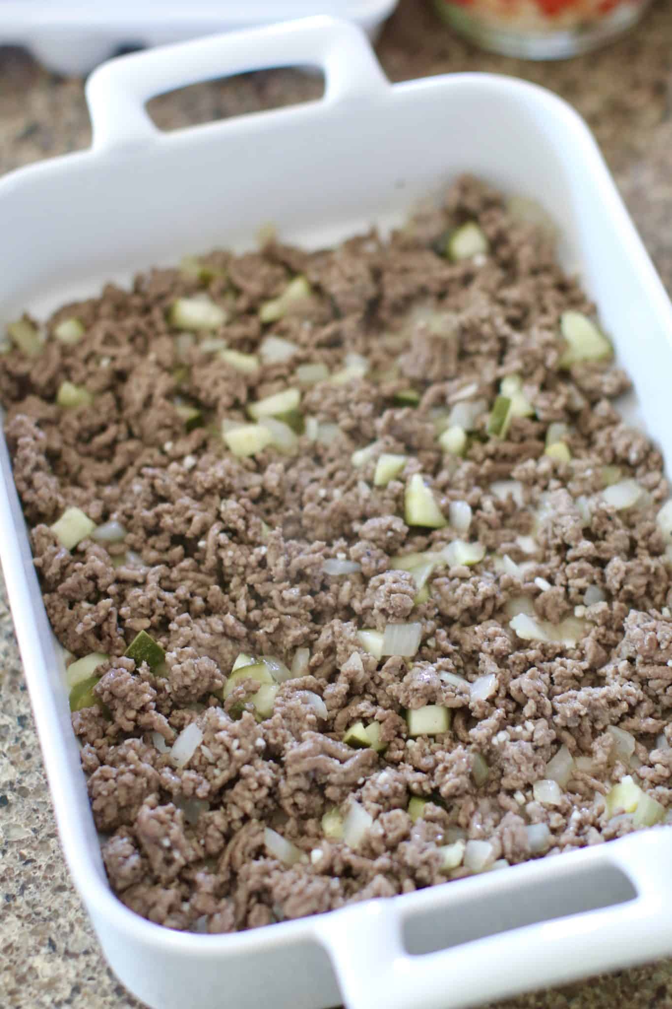 cooked ground beef mixture layered evenly into the bottom of a white baking dish.
