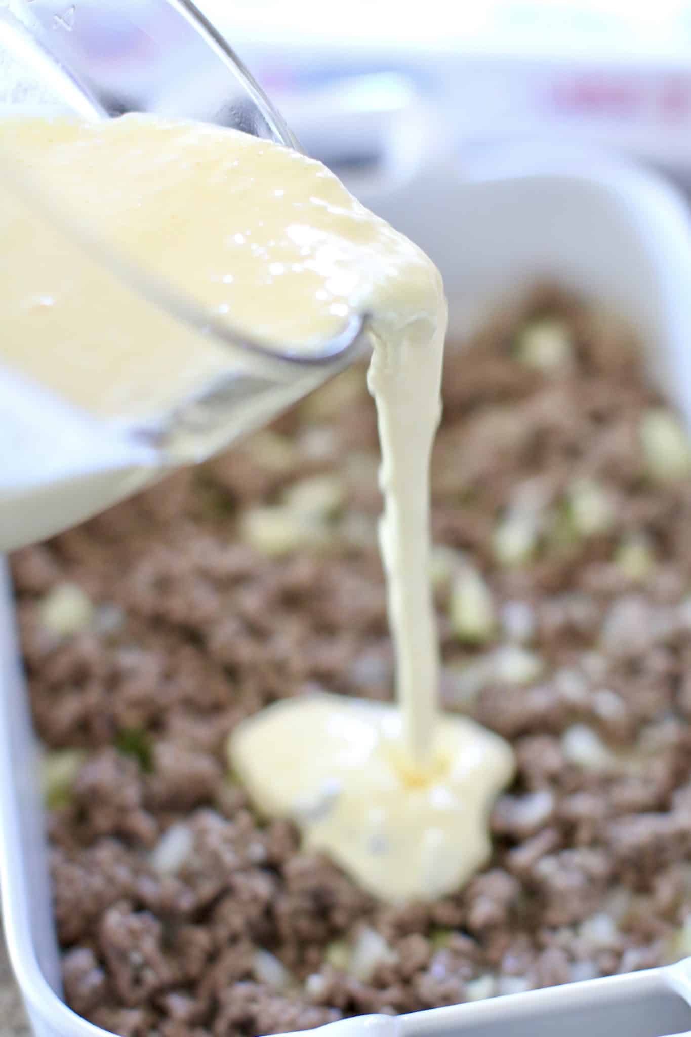 egg and heavy cream mixture pouring over ground beef in a casserole dish.