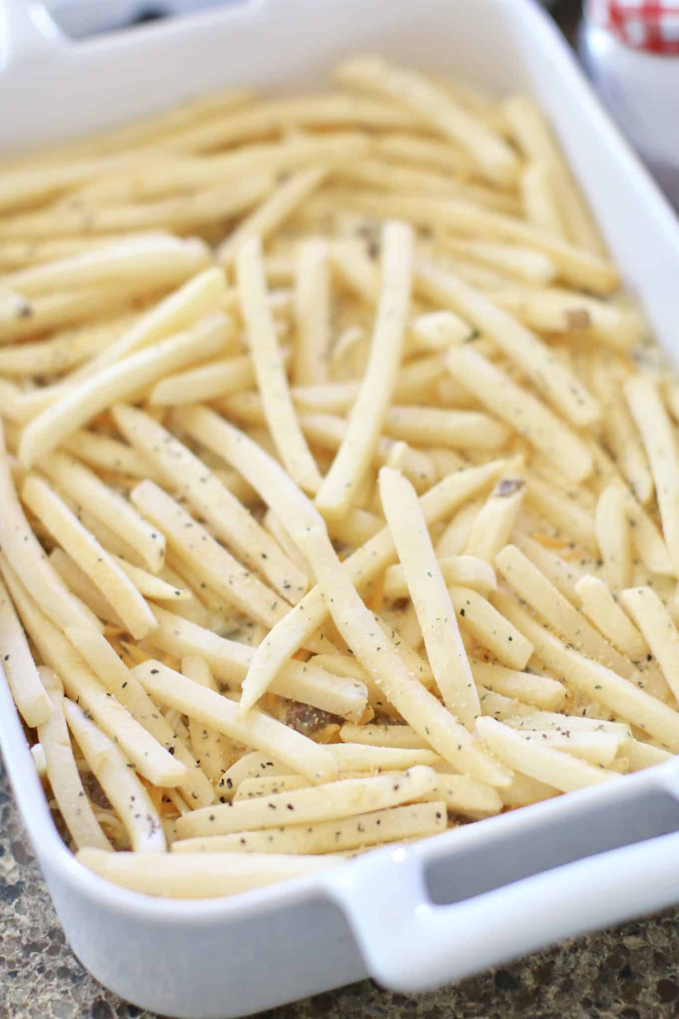 frozen French fries spread evenly on top of ground beef in a baking dish.