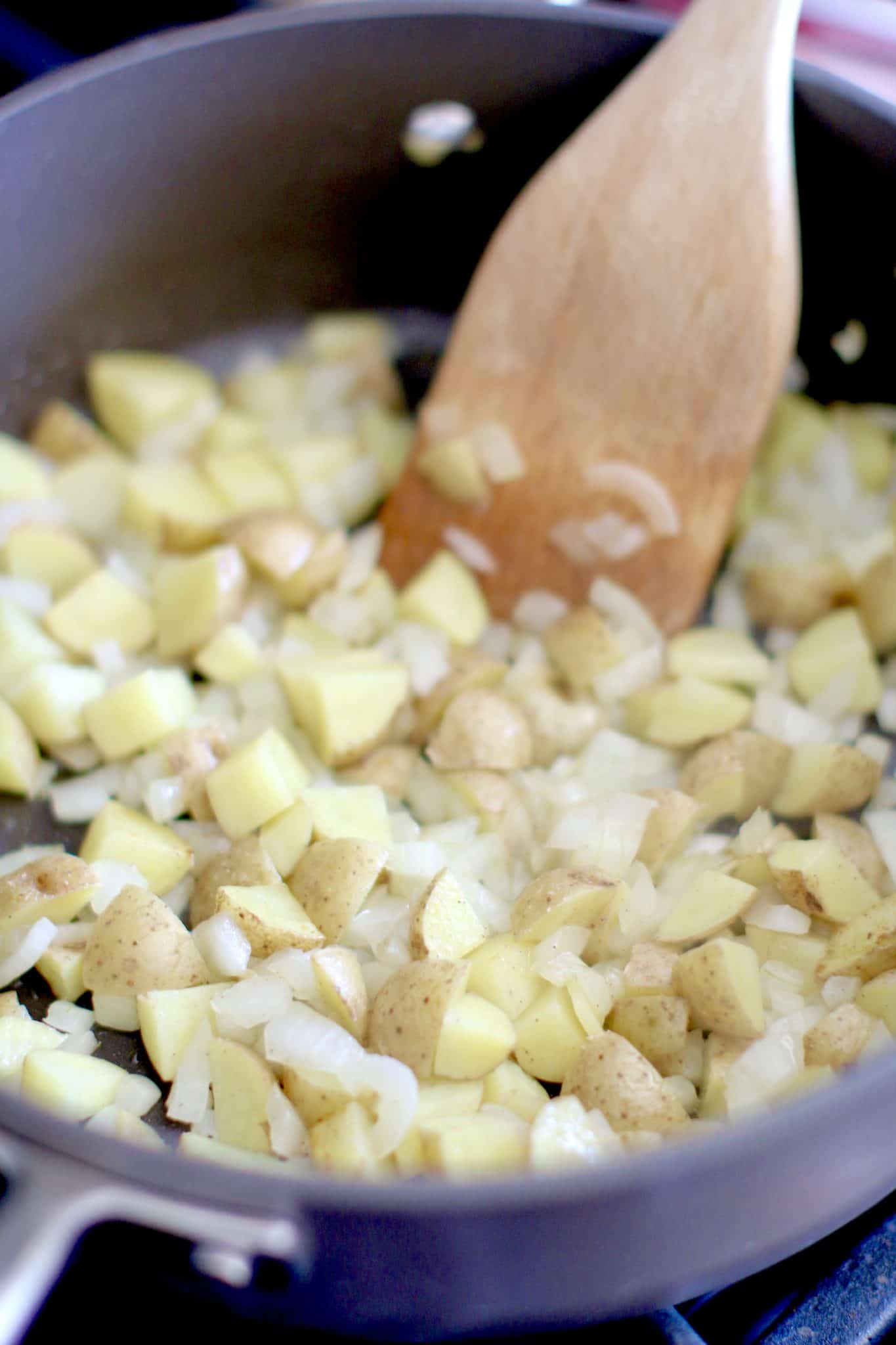 diced potatoes and onions in a skillet with a wooden spatula.