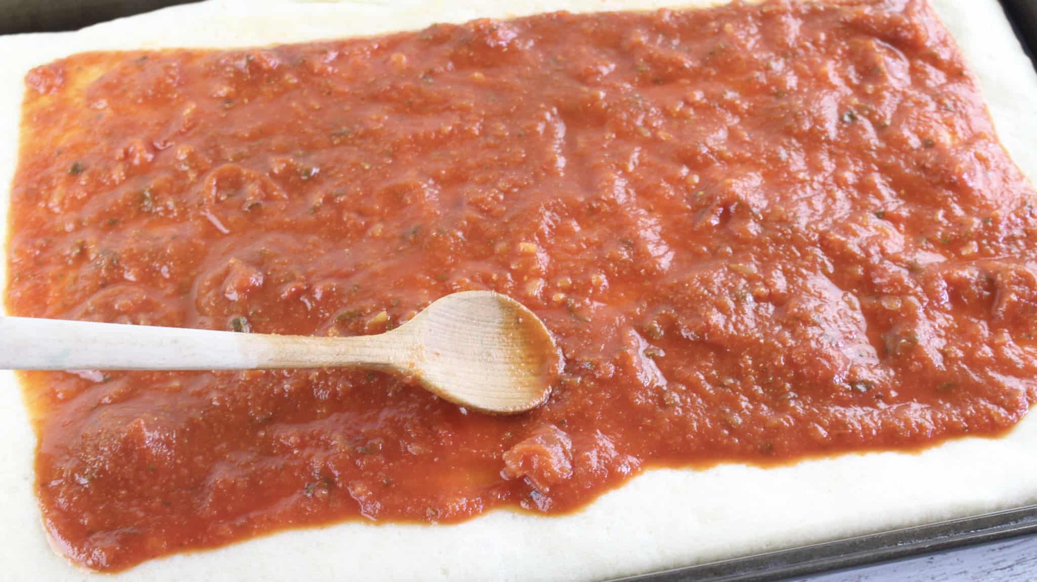 marinara sauce being spread evenly over pizza dough. 