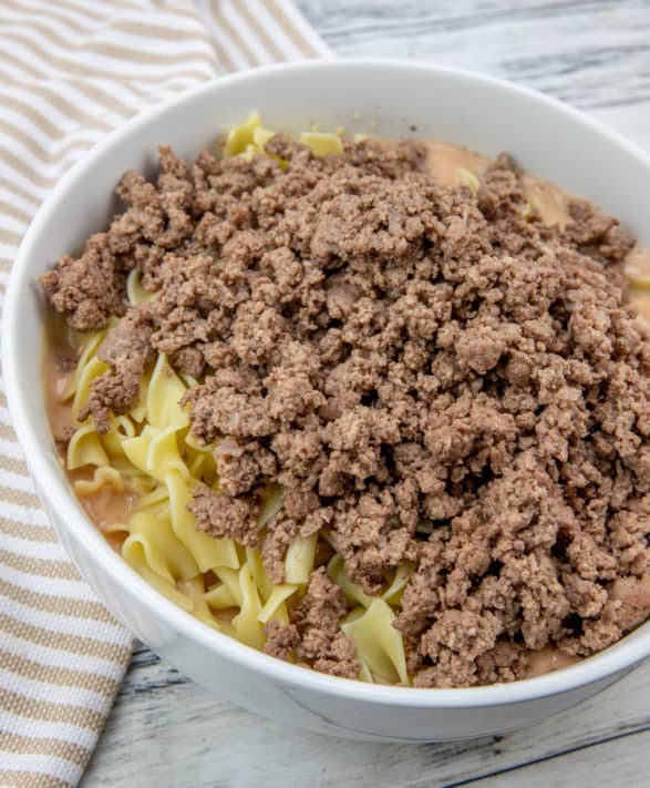cooked ground beef stirred in with cooked egg noodles in a bowl.