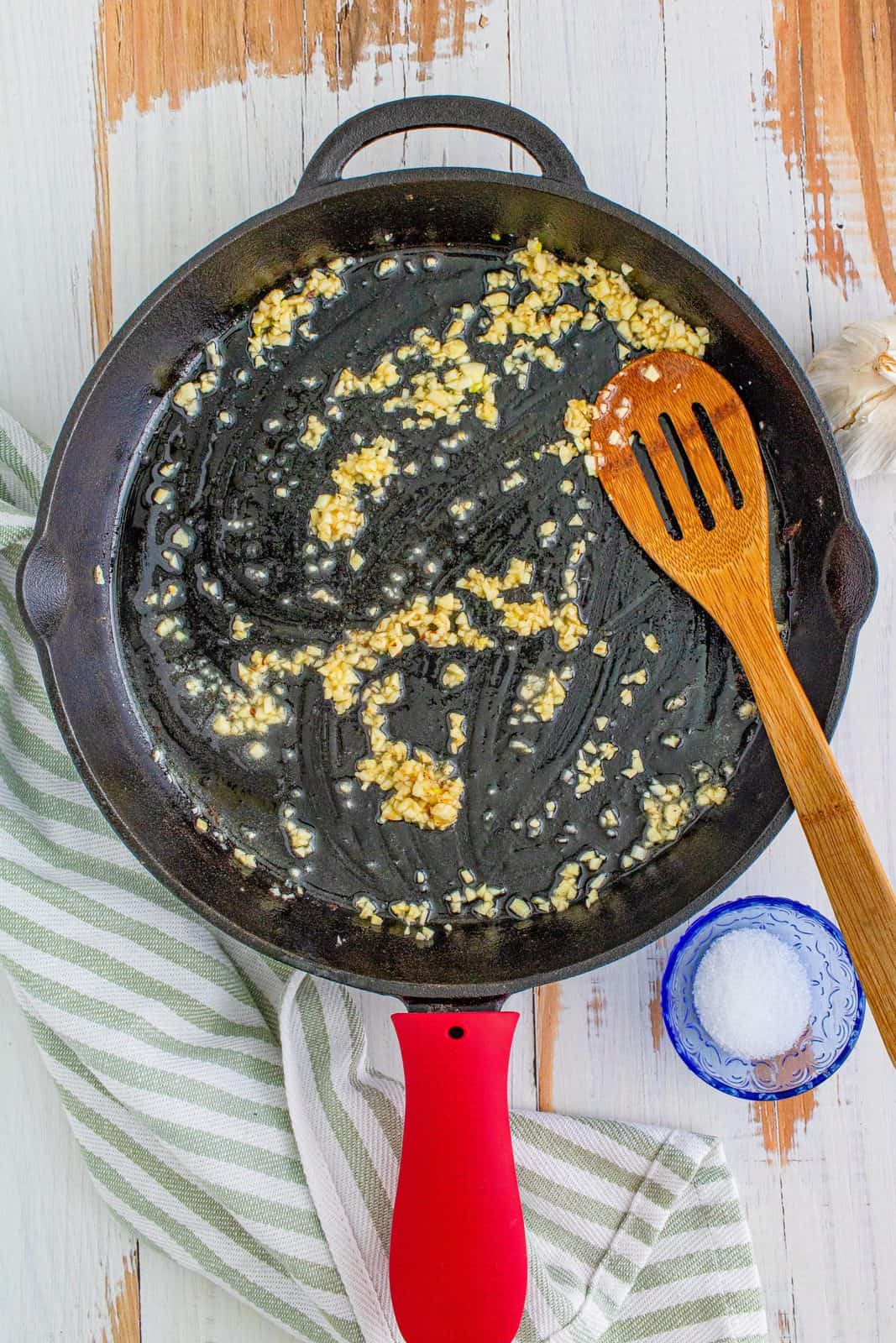 bacon grease, melted butter and minced garlic shown in a cast iron skillet with a wooden spatula.