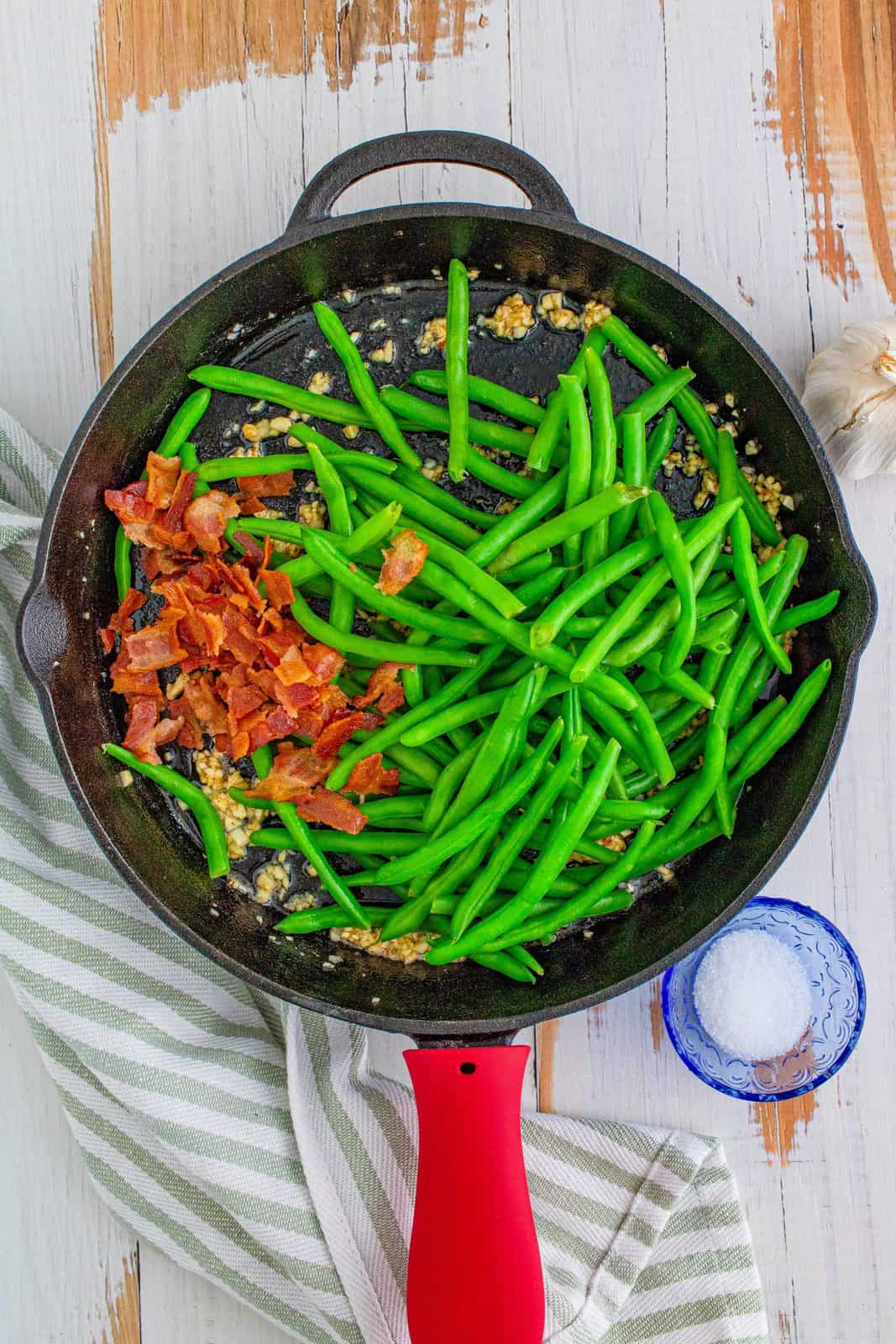 crumbled bacon and cooked green beans added into the cast iron skillet with minced garlic