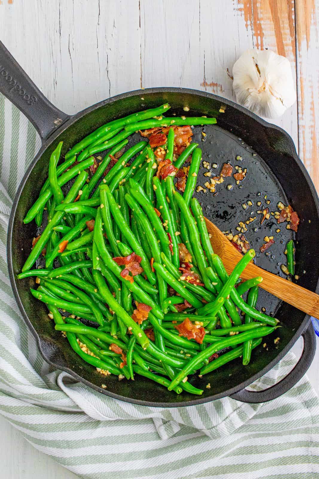 fully cooked green beans and bacon in a cast iron skillet.