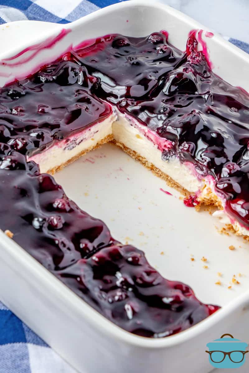 fully cooled blueberry cream cheese bars shown in white pan with two pieces removed.