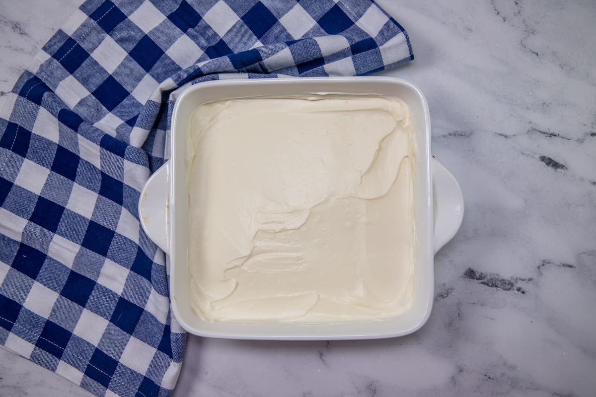sweetened cream cheese spread over vanilla wafer crust in white square baking dish.