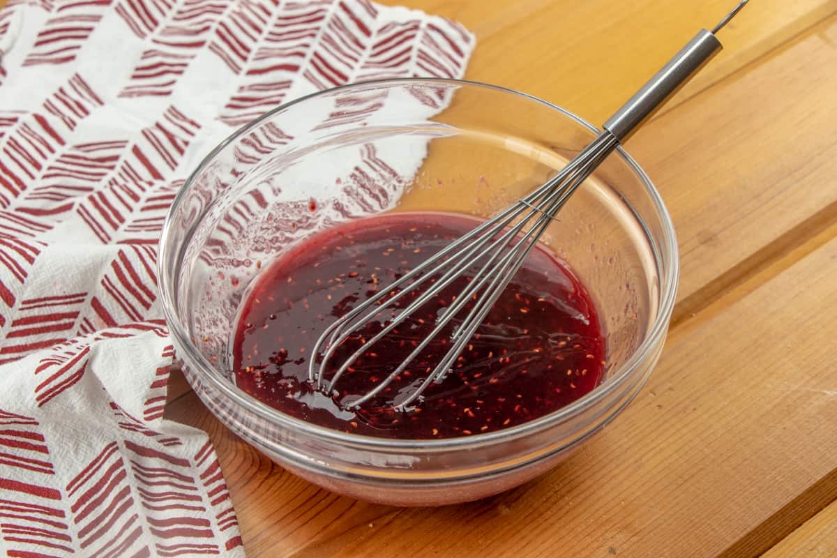 whisking together raspberry preserves with water in a clear bowl.