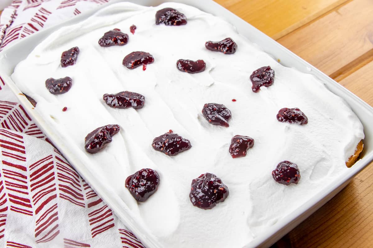 raspberry preserves dolloped on whipped cream on top of lemon cake.