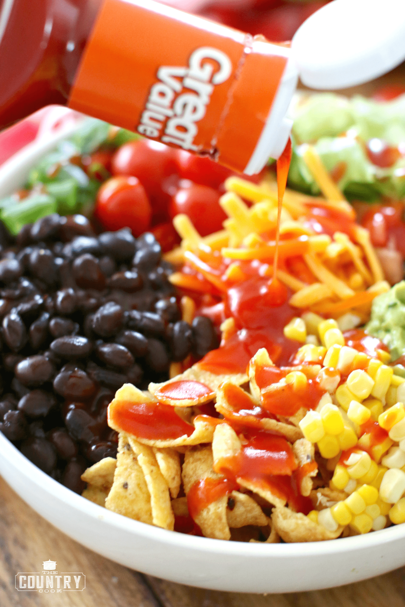 Pouring French dressing over Vegetarian Taco Salad.