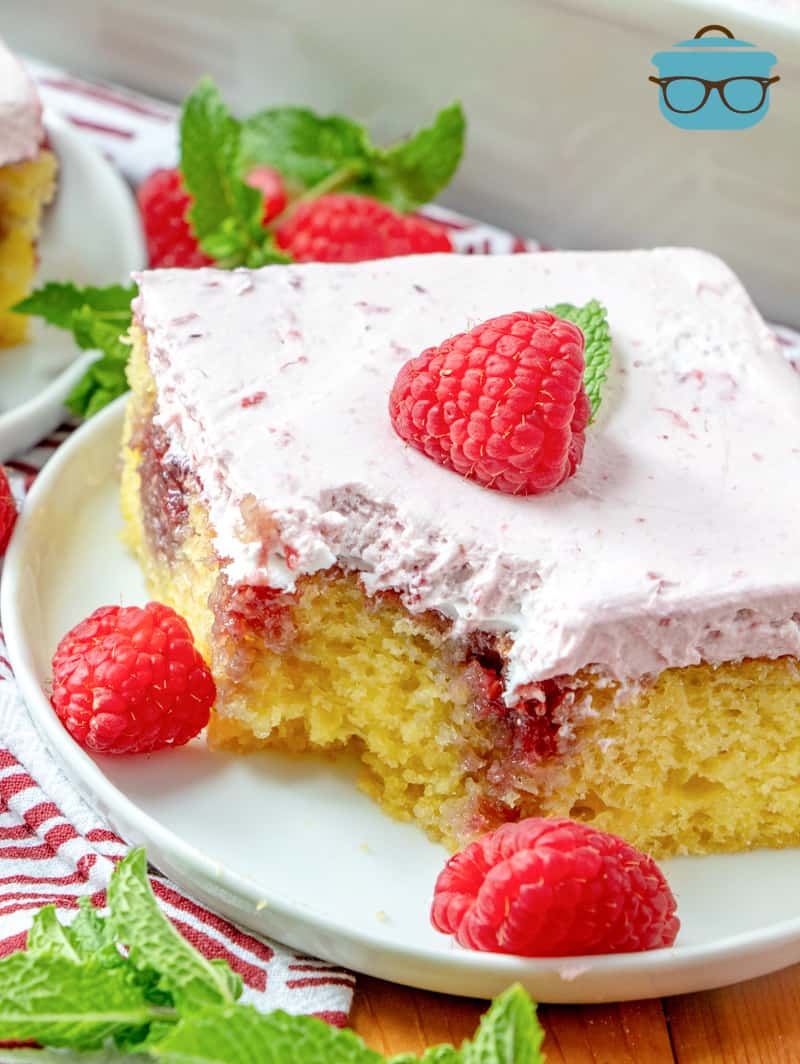 slice of Lemon Raspberry Poke Cake on a white plate with a bite cut out.
