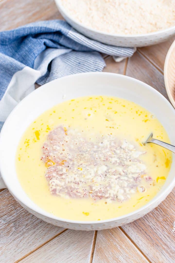 flour covered cubed steak dipped into egg mixture in a shallow white bowl.