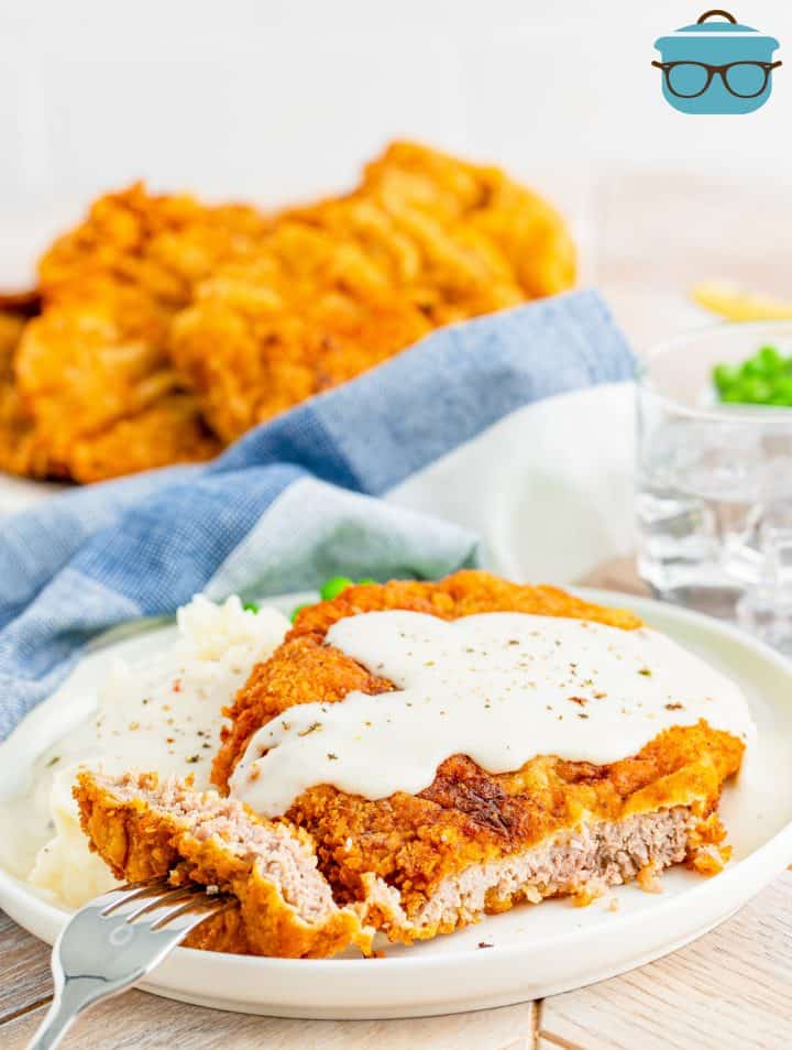 chicken fried steak on a white plate with a slice cut out.