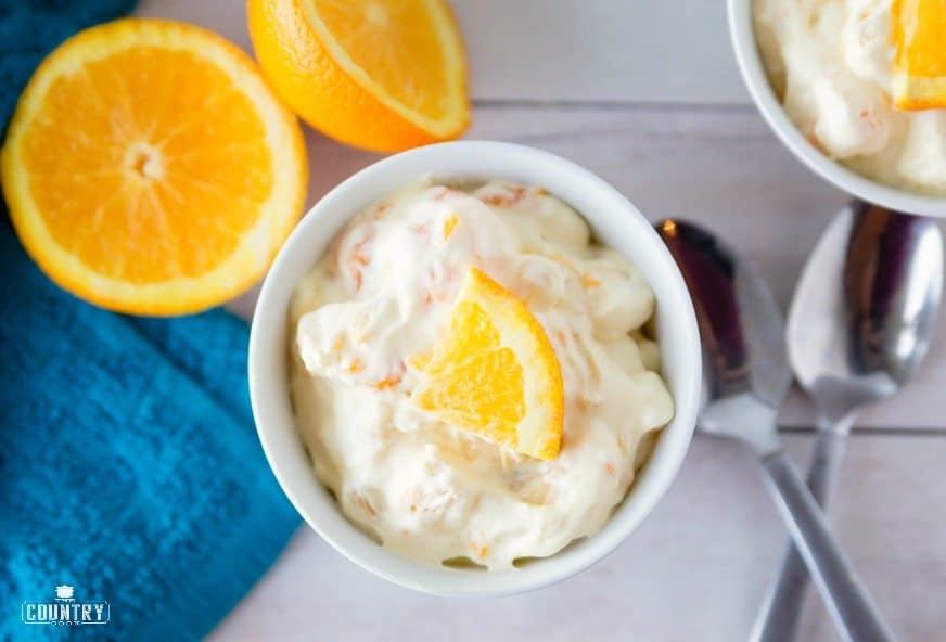 creamsicle salad in a bowl with fresh oranges shown in a white bowl.