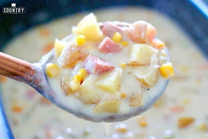 Potatoes, ham, corn and carrots in chowder being helped up by a wood ladle.