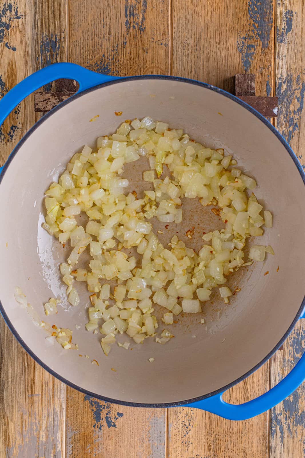 diced yellow onions being cooked in a blue dutch oven. 