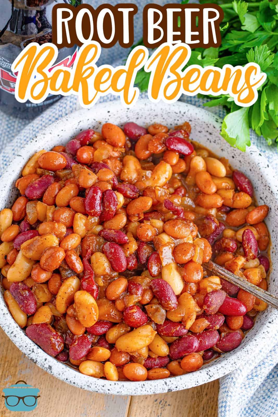 overhead photo of a bowl of root beer baked beans with a spoon inserted into the beans and a bottle of root beer in the background. 