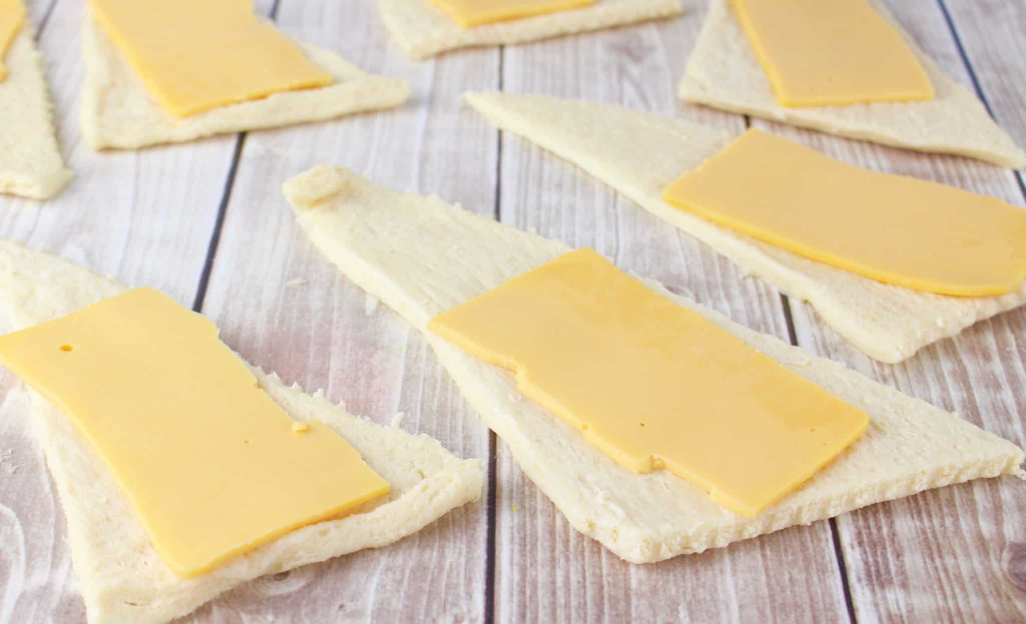 slices of American cheese place on crescent roll triangles.