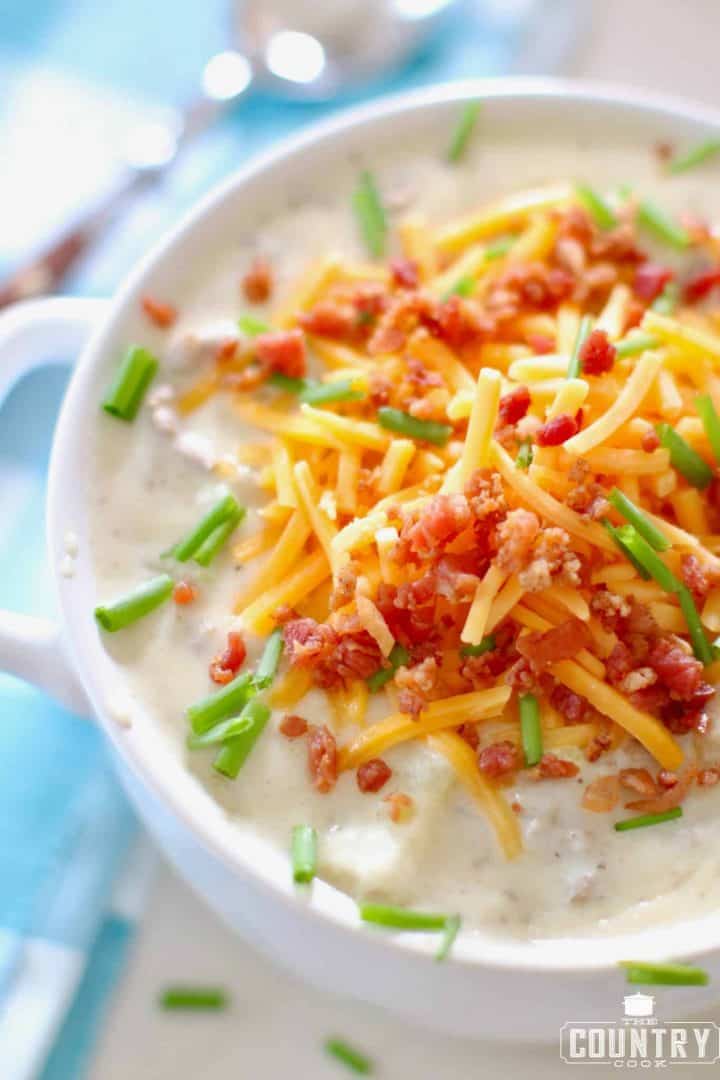 creamy hamburger and potato soup in a bowl topped with shredded cheddar cheese, bacon and chives.