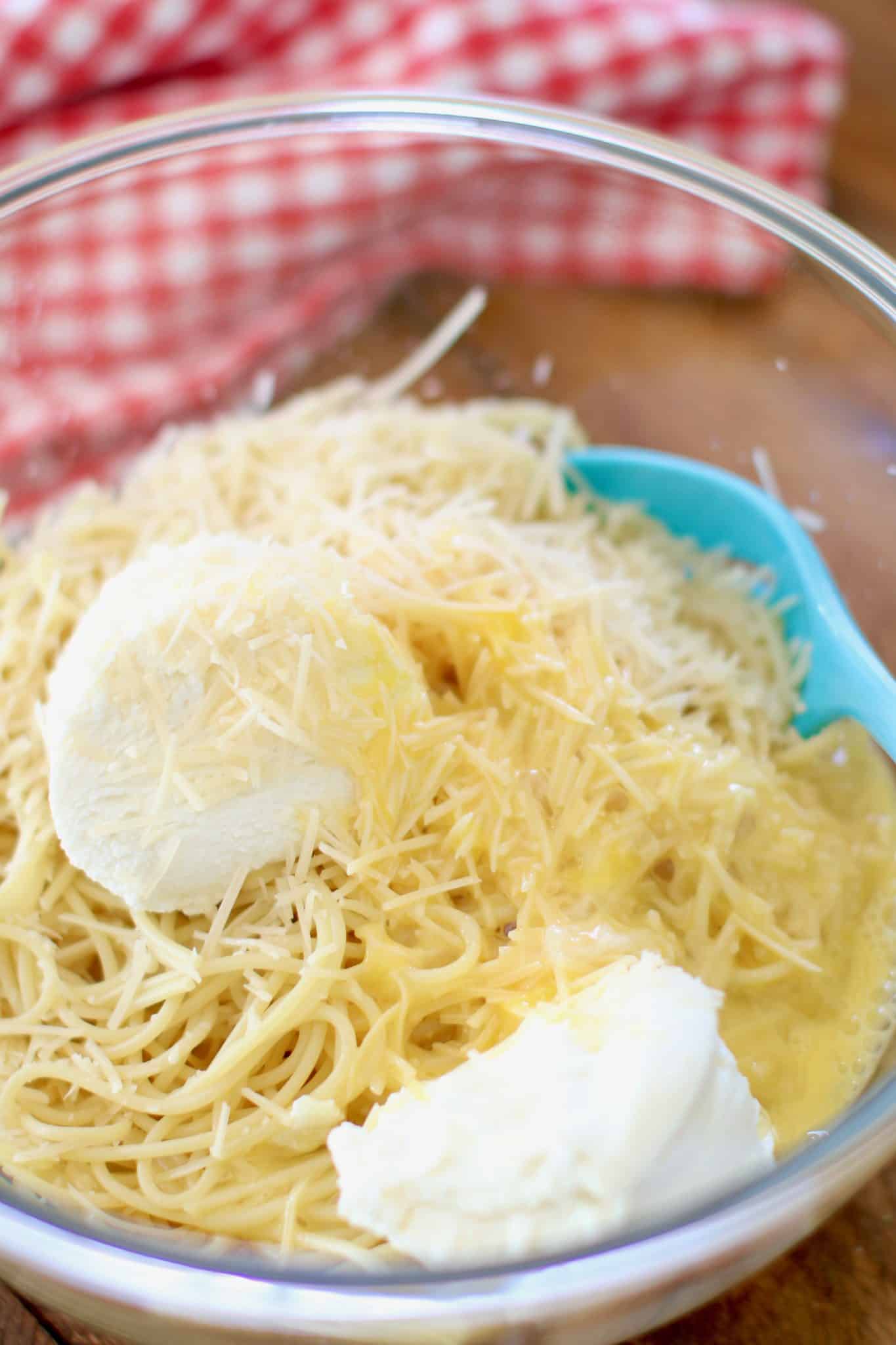 cooked spaghetti, ricotta cheese, Parmesan cheese and beaten eggs in a large glass bowl.