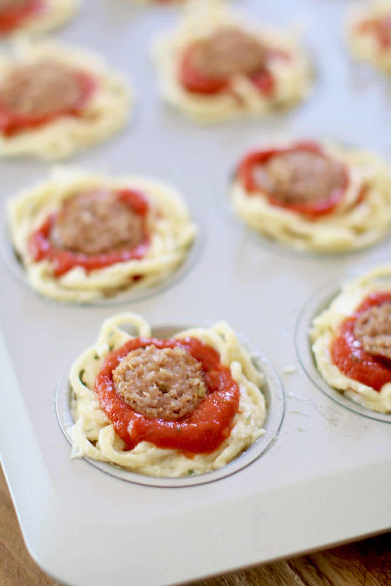spaghetti nests, spaghetti sauce and sliced sausage in a muffin pan (before baking).