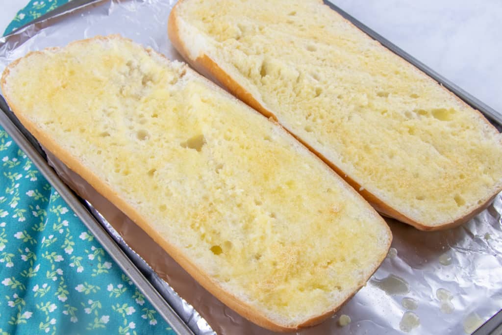 melted butter spread onto a loaf of Italian bread that has been sliced in half and put onto a large baking sheet