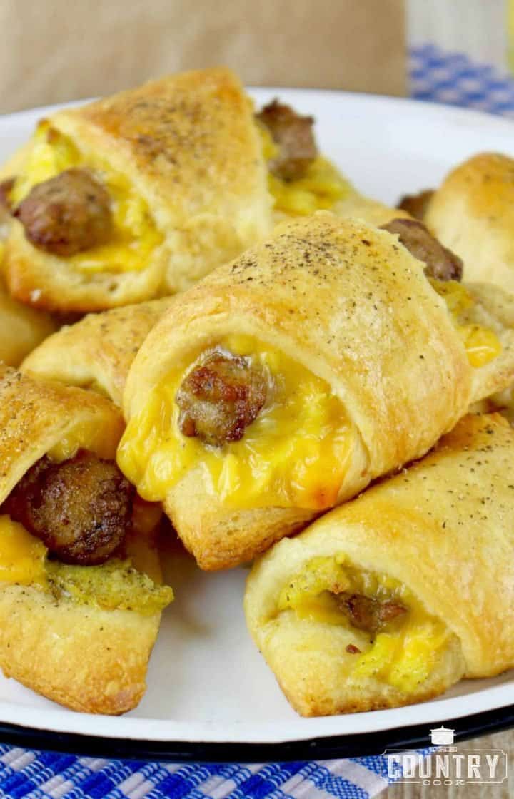 closeup photo of stacked sausage, egg and cheese breakfast rolls on a white plate.