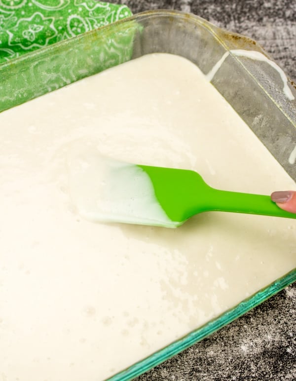 a green spatula smoothing cake mix batter in a glass baking dish. 