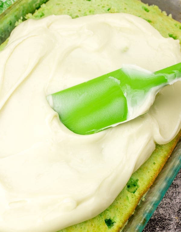 spreading key lime pie filling with a green spatula over the key lime poke cake. 