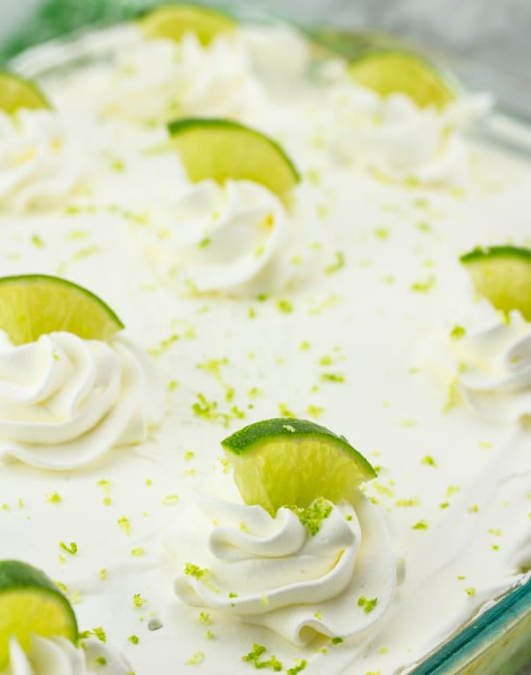 lime wedges and fresh lime zest shown on frosted key lime poke cake. 