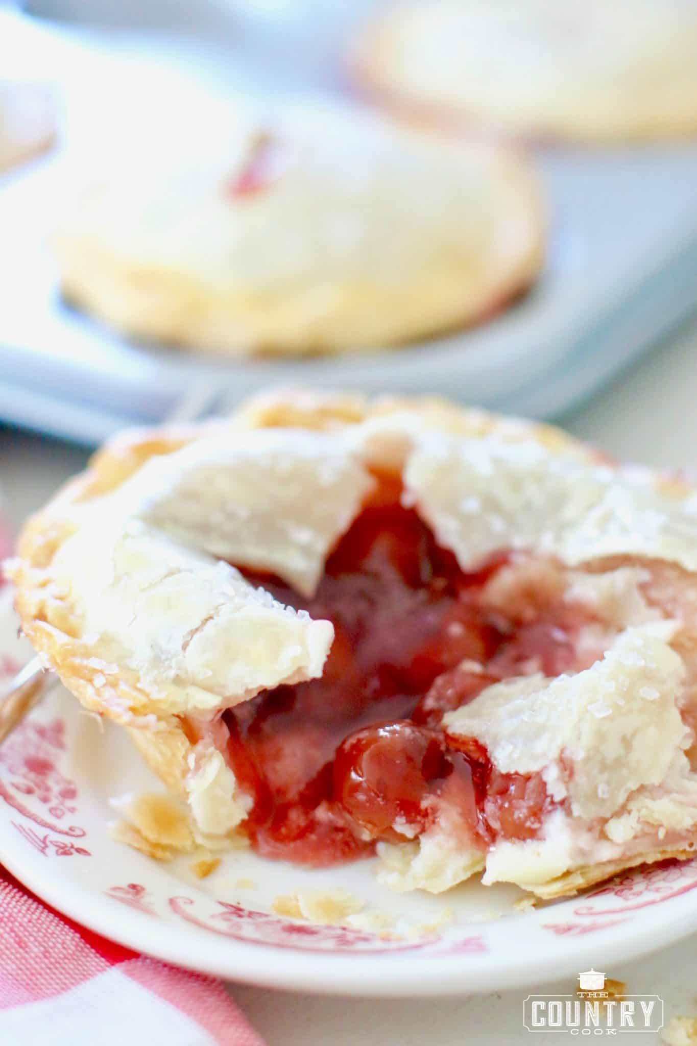 a mini cherry pie on a plate and the pie has been opened to show the filling.