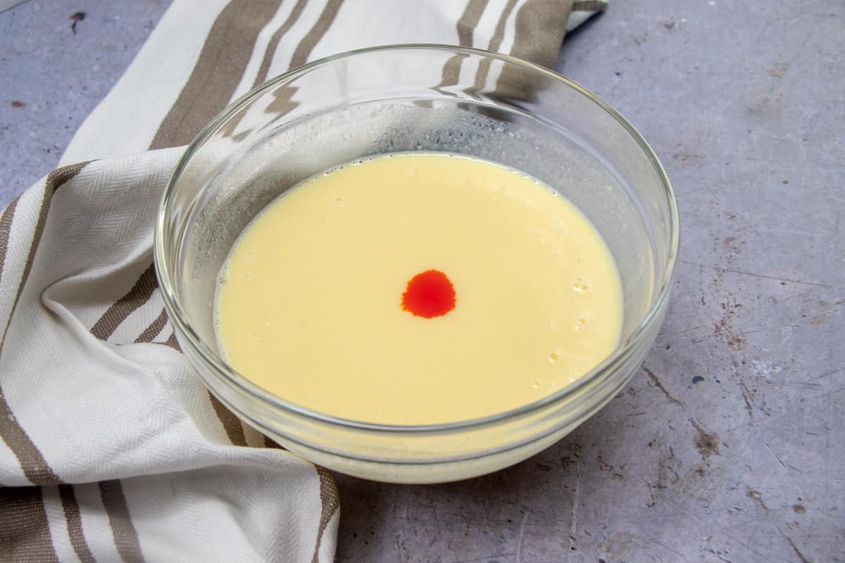 ORANGE FOOD COLORING, VANILLA PUDDING AND COLD MILK MIXED TOGETHER IN A CLEAR BOWL.
