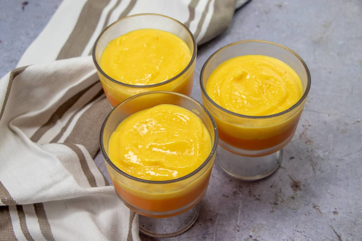 YELLOW COLORED VANILLA PUDDING SPOONED ON TOP OF ORANGE COLORED VANILLA PUDDING IN GLASS DESSERT Glasses.