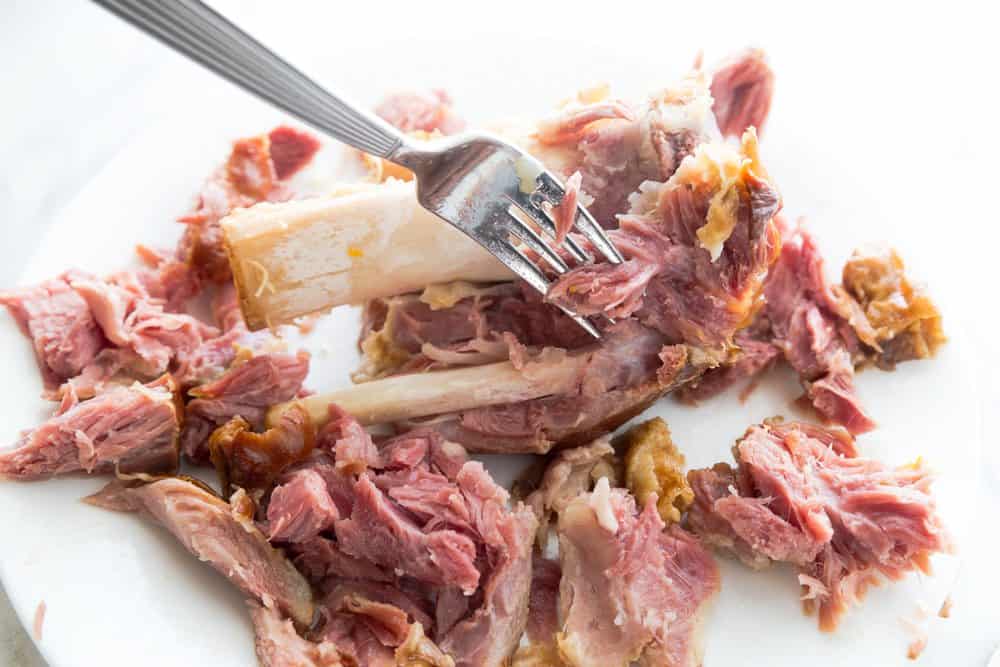 a fork shredding ham hock meat off the bone.
