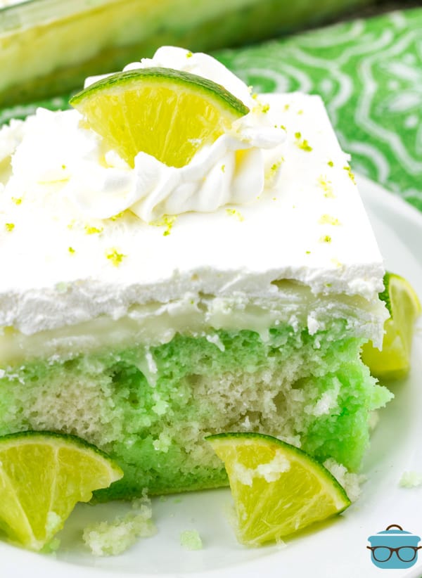 a closeup photo of a slice of Key Lime Poke Cake on a small white plate with little wedges of fresh lime. 