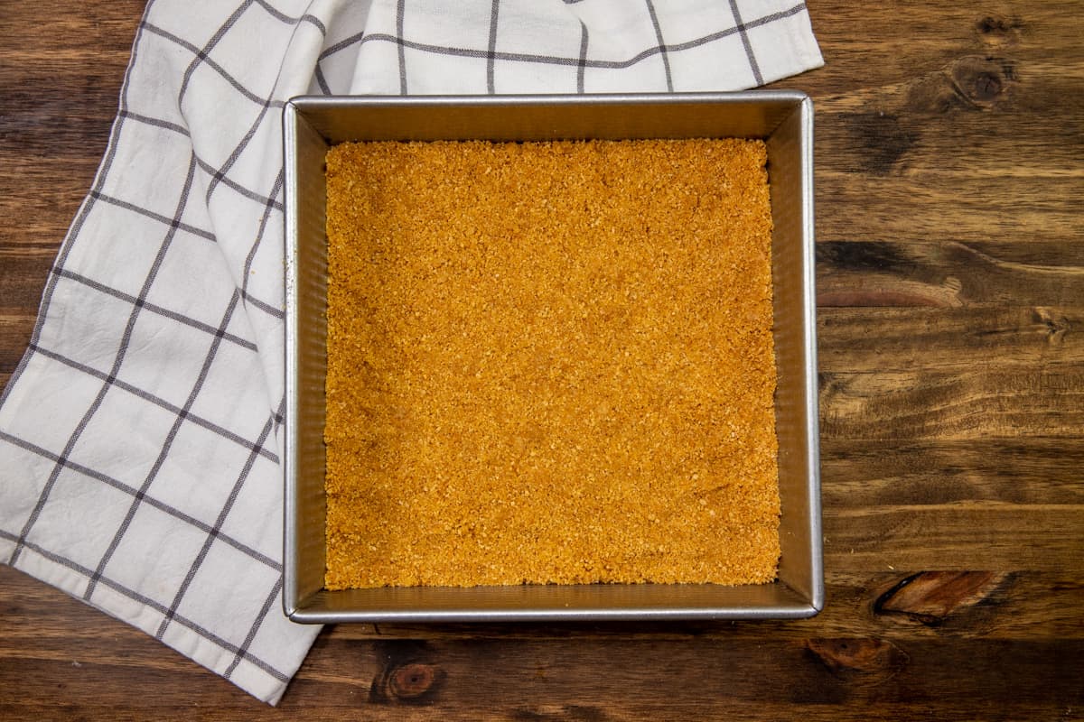 graham cracker crust mixture spread into the bottom of a 9 by 9 inch metal baking pan.