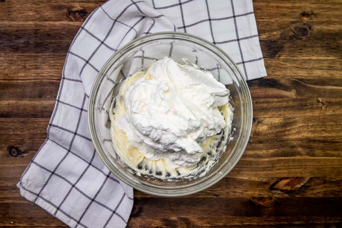 fresh, homemade whipped cream poured on top of cream cheese mixture in a bowl.